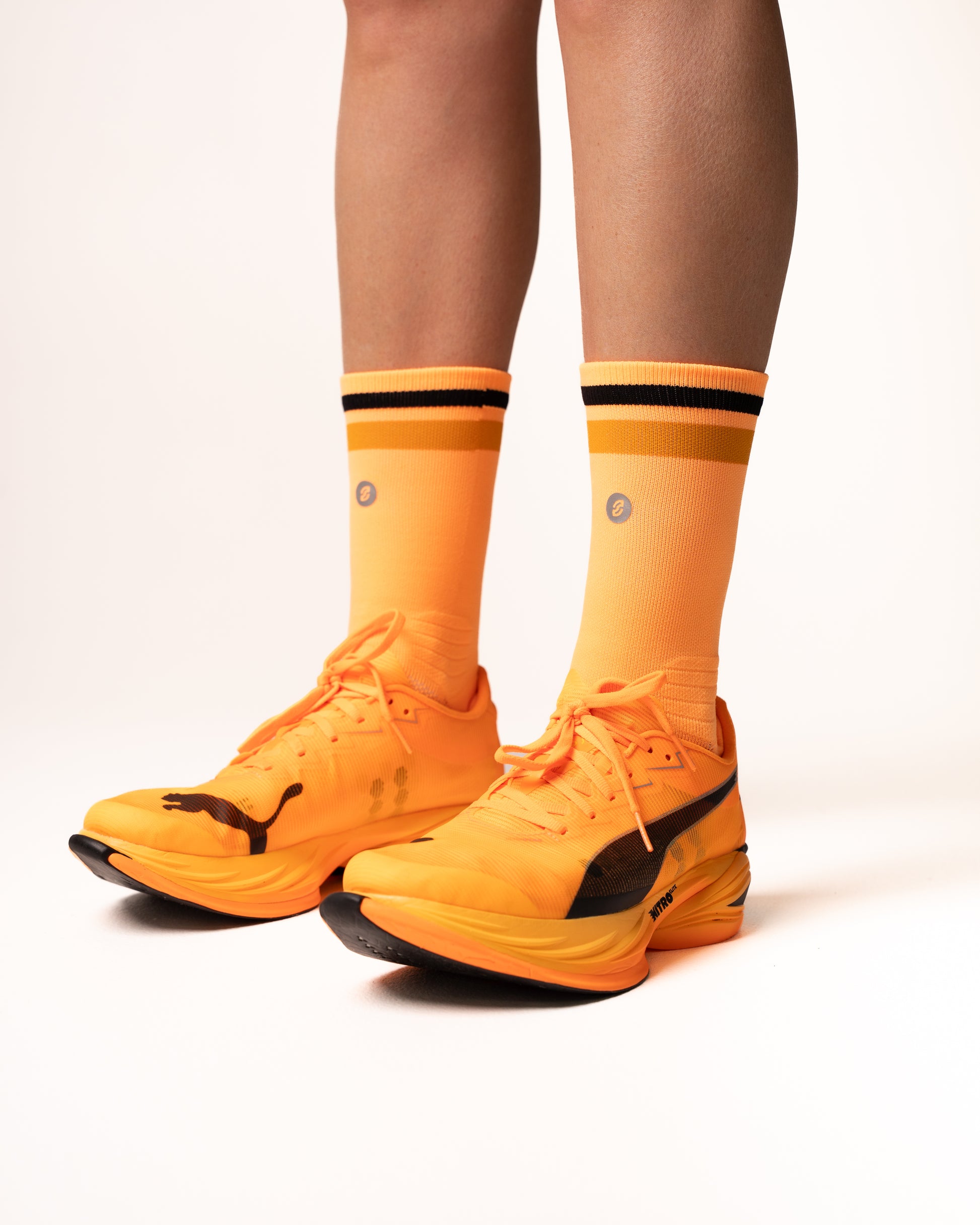 Orange athletic shoes with black accents worn by a person on a white background